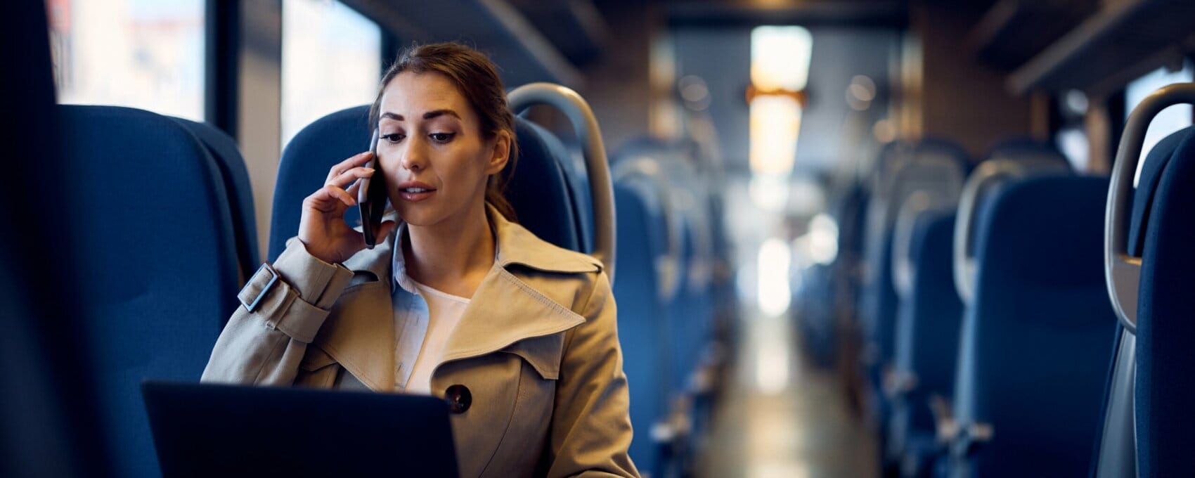Office worker on train whilst speaking on mobile and looking at laptop